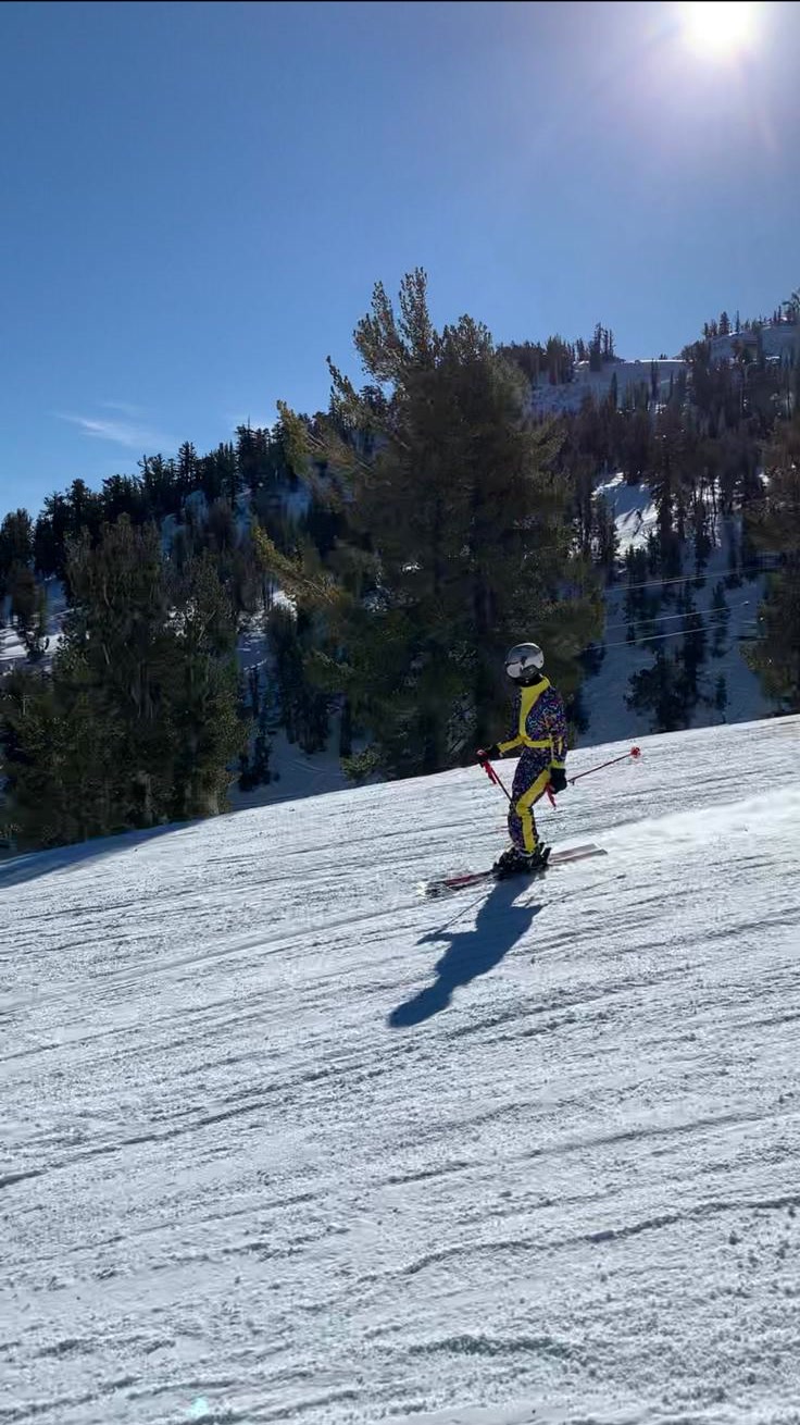 A young skier in a helmet and bright snowsuit standing on a groomed beginner slope